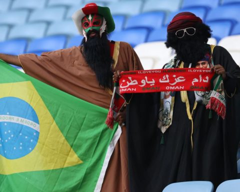 Dos aficionados posan con una bandera de Brasil y una bufanda de Omán en el partido entre Irak y Omán, en el estadio Al Janoub.