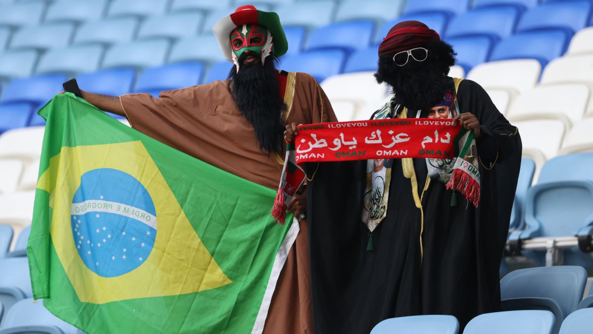 Dos aficionados posan con una bandera de Brasil y una bufanda de Omán en el partido entre Irak y Omán, en el estadio Al Janoub.