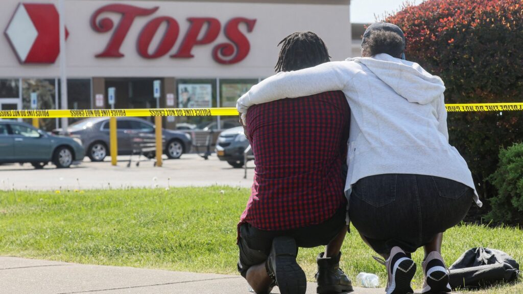 Dos personas se abrazan agachadas mientras miran hacia un supermercado de la localidad estadounidense de Búfalo, en Nueva York, donde un tiroteo causó la muerte a 10 personas el 14 de mayo de 2022. Foto: Brendan McDermid / Reuters / gazette.com