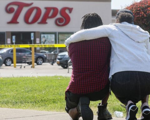 Dos personas se abrazan agachadas mientras miran hacia un supermercado de la localidad estadounidense de Búfalo, en Nueva York, donde un tiroteo causó la muerte a 10 personas el 14 de mayo de 2022. Foto: Brendan McDermid / Reuters / gazette.com