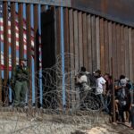 Migrantes centroamericanos miran a través de la valla mientras un agente de la Patrulla Fronteriza vigila cerca del cruce fronterizo de El Chaparral en Tijuana, México (2018). Foto: tomada de The New York Times.
