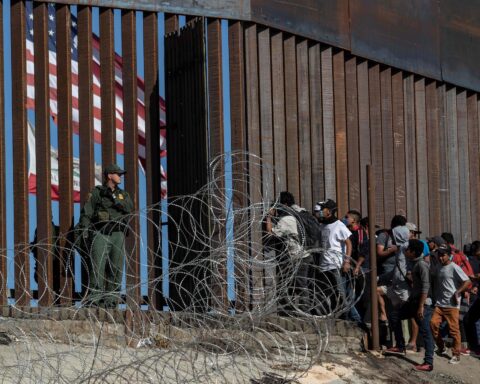 Migrantes centroamericanos miran a través de la valla mientras un agente de la Patrulla Fronteriza vigila cerca del cruce fronterizo de El Chaparral en Tijuana, México (2018). Foto: tomada de The New York Times.