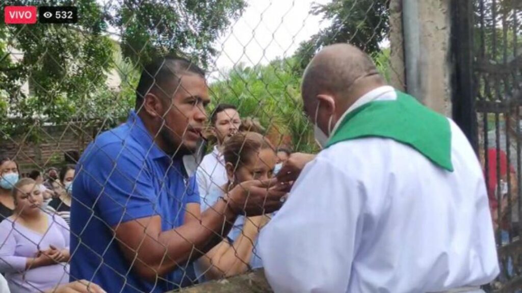 Priest officiates mass through a mesh before police blockade