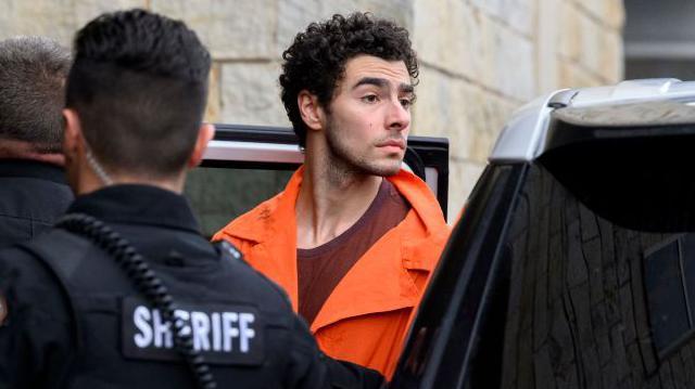 Luigi Mangione, the man accused of murdering UnitedHealth CEO Brian Thompson, arrives for a hearing in a Pennsylvania court. He wears an orange prison uniform.