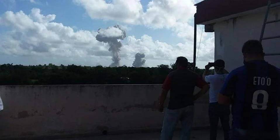 Tres personas observan la columna de humo provocada por la explosión en el almacén militar de Melones, en Holguín, Cuba