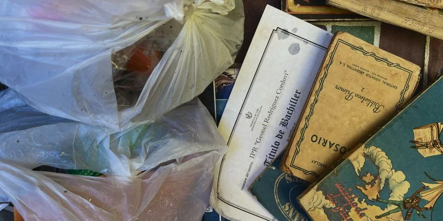Un título de bachiller junto a varios libros y bolsas de basura