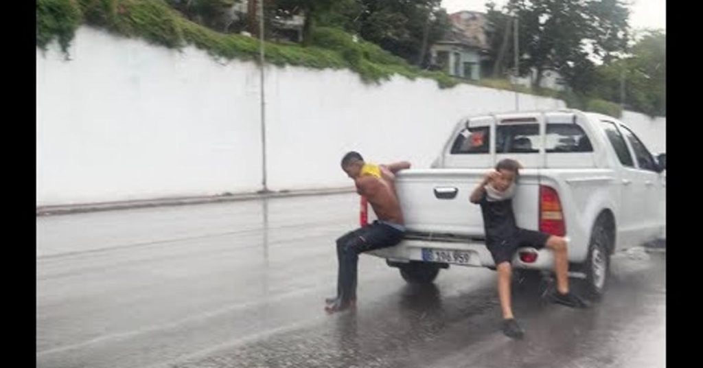 Danger in the streets! Children cling to cars during rains in Havana