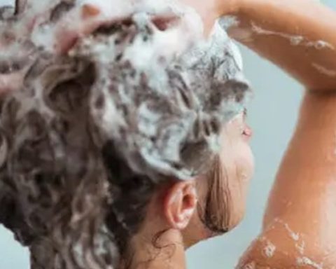 Mujer echándose shampoo en el baño.