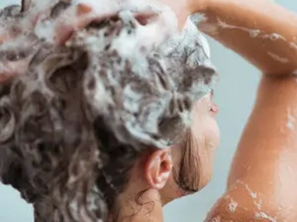 Mujer echándose shampoo en el baño.