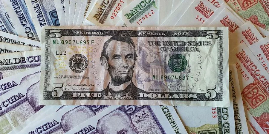 Un billete de cinco dólares sobre decenas de billetes de pesos cubanos